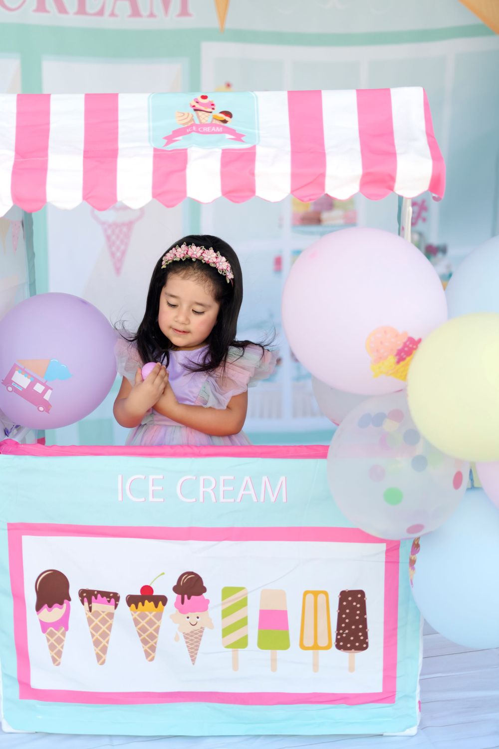 A charming ice cream shop setup with pastel balloons and a pink striped awning for a children's photoshoot.