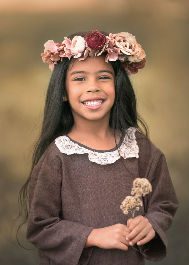 Young child wearing flower crown and brown dress in outdoor portrait.