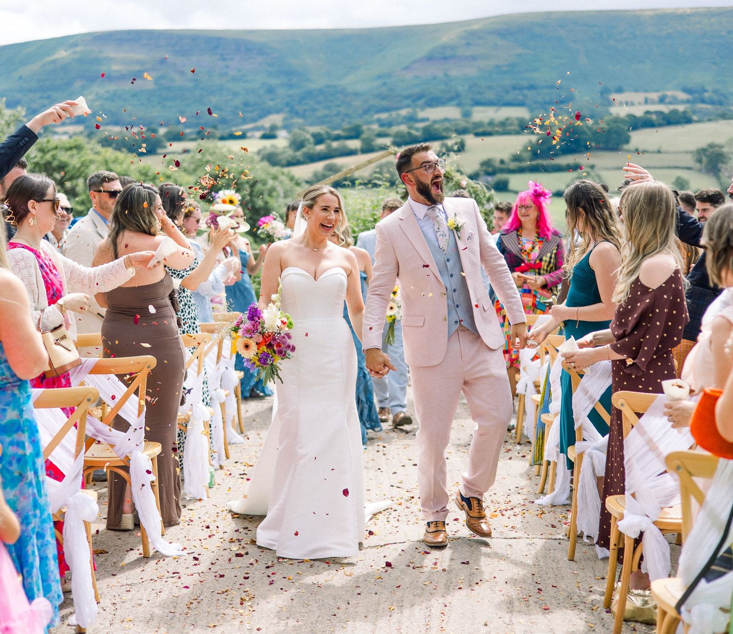 Wedding guests in light summer attire gather for outdoor hillside celebration.