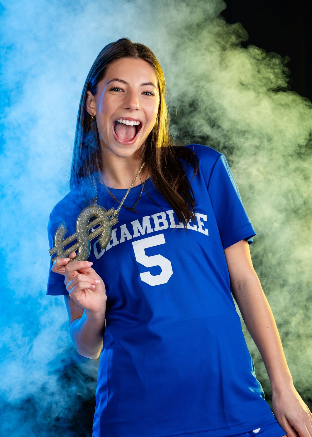 Athlete in blue team jersey smiling energetically against colorful smoke backdrop during sports photoshoot.