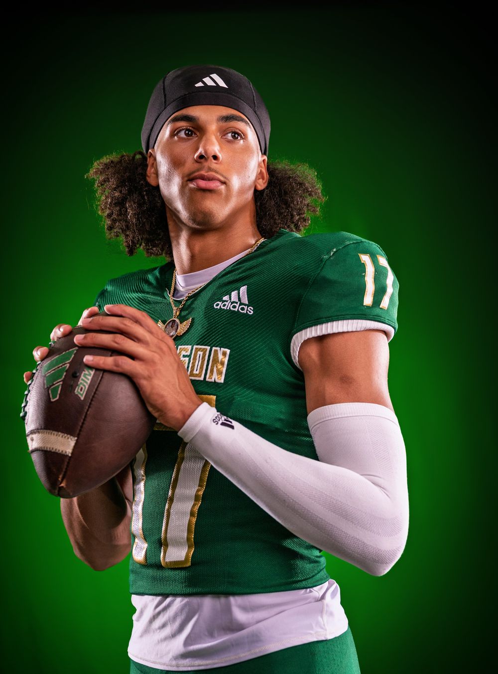 Athletic figure in green and white football uniform #11 poses with football against emerald background.