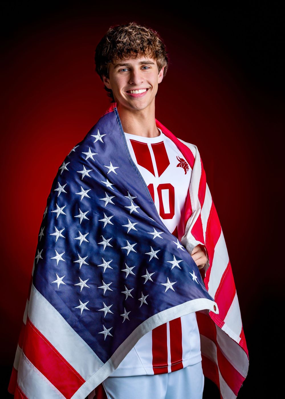 Student athlete draped in American flag poses against red backdrop wearing sports jersey with number 10.