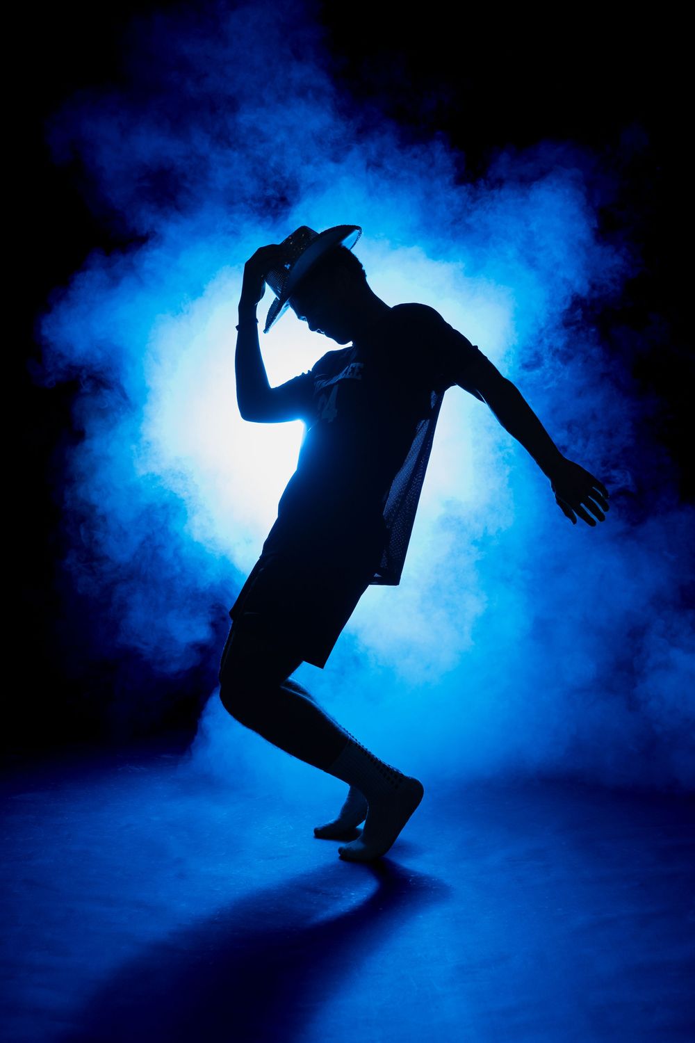 Silhouette of a dancer striking a dramatic pose against a backlit blue smoky background.