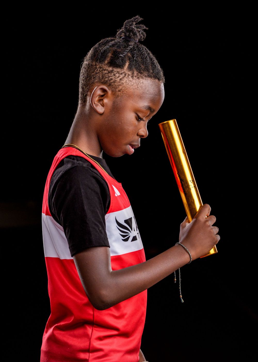 Young athlete in a red and black jersey uniform holds a golden relay race baton against a dark background.