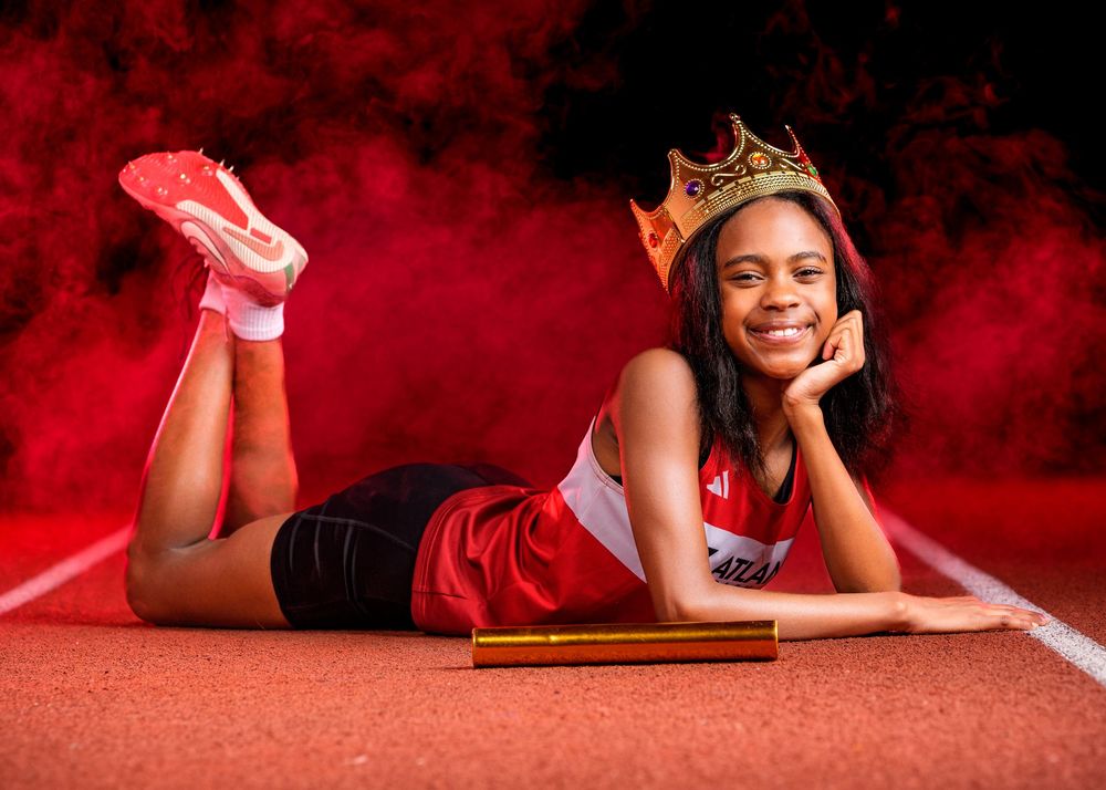 Athletic figure in red outfit and crown poses on running track with dramatic red smoke background.