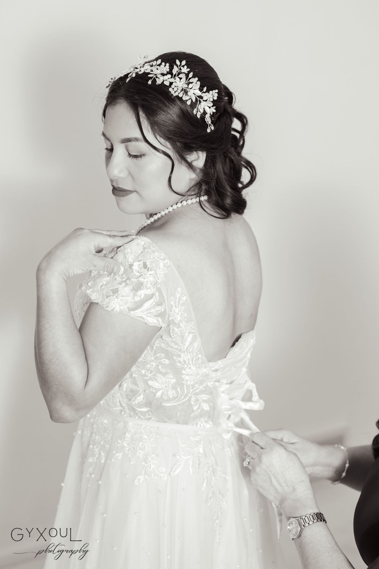 A black and white portrait showing intricate lace details and floral hairpiece on wedding dress.