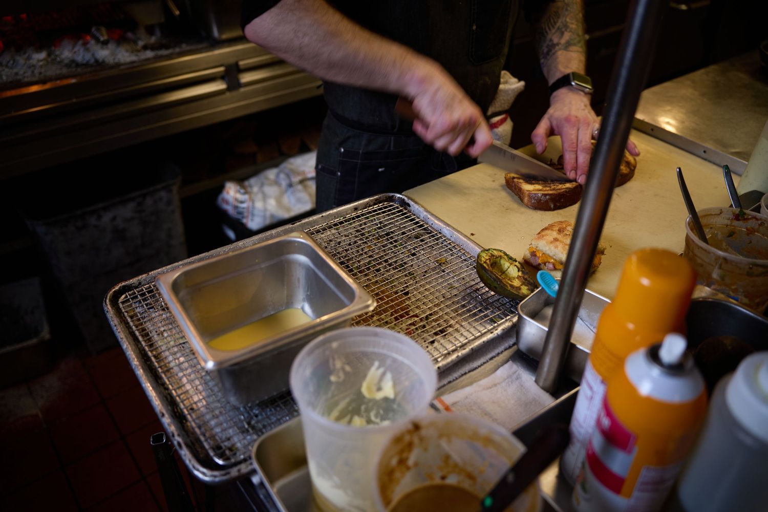 A close-up shot of hands preparing food at a professional cooking station with metal prep containers and tools.