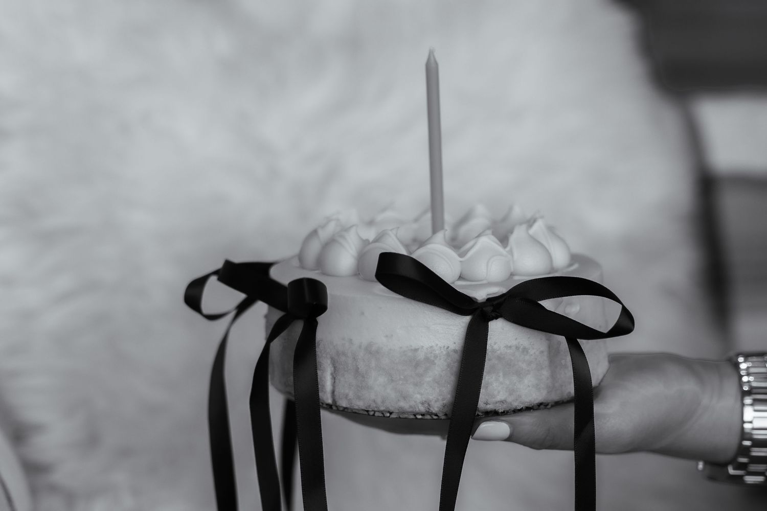 A white cupcake decorated with black ribbons and a candle sits ready for celebration.