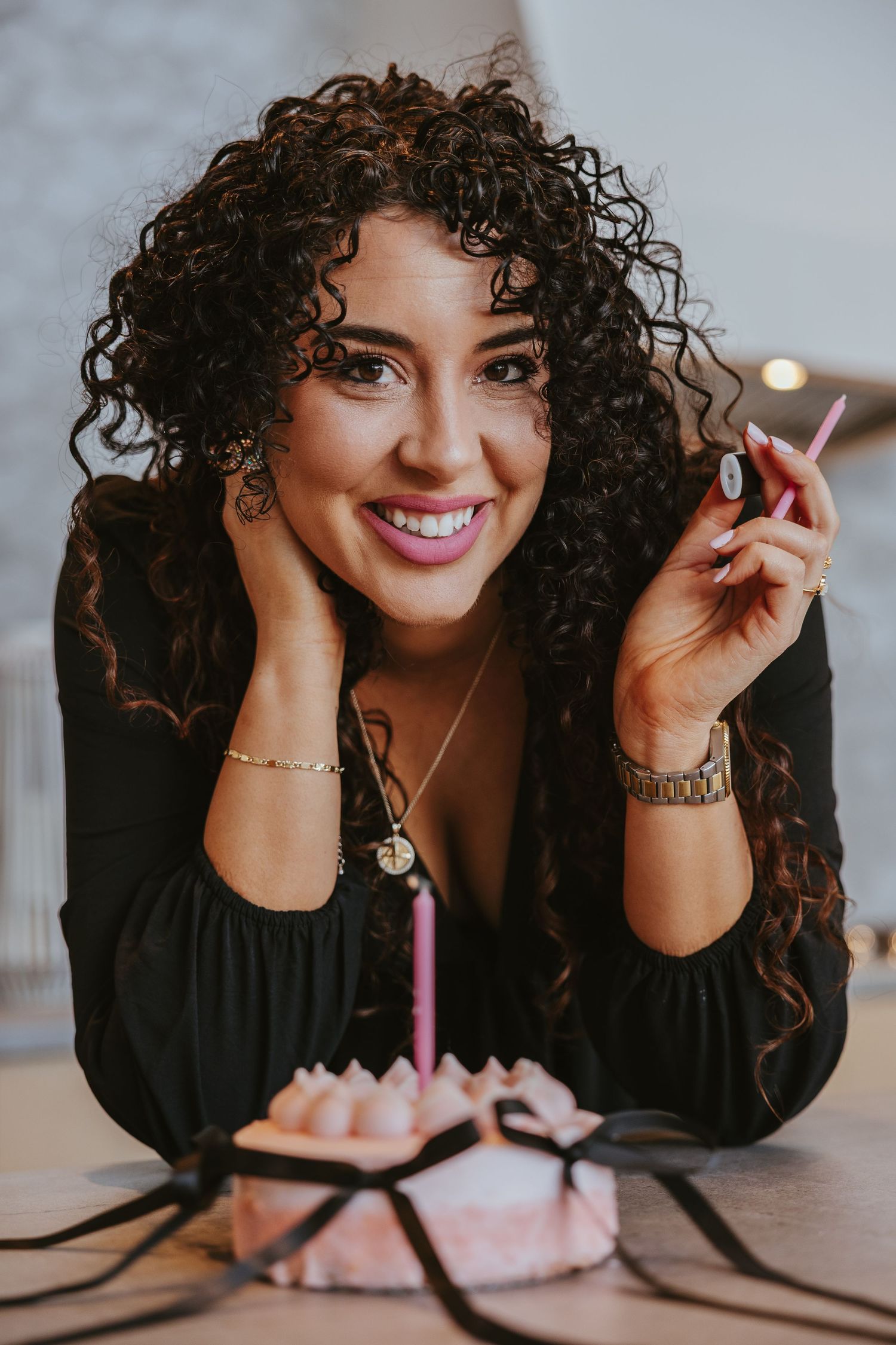 Woman in black top with curly hair poses with a birthday cupcake and candle.