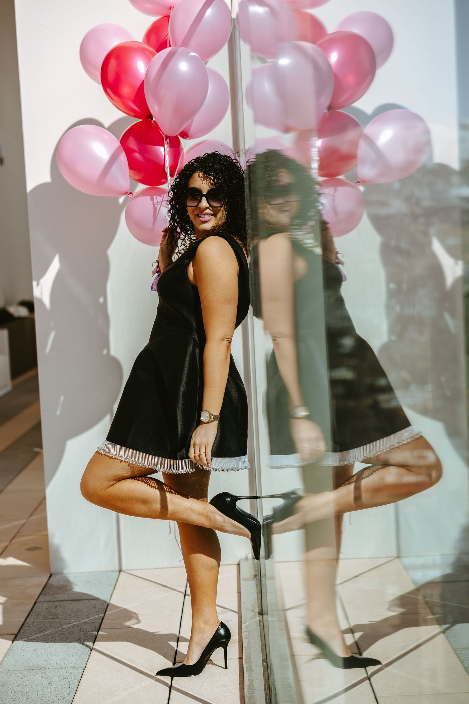Fashion portrait in black dress with pink and red balloons reflecting in mirror.