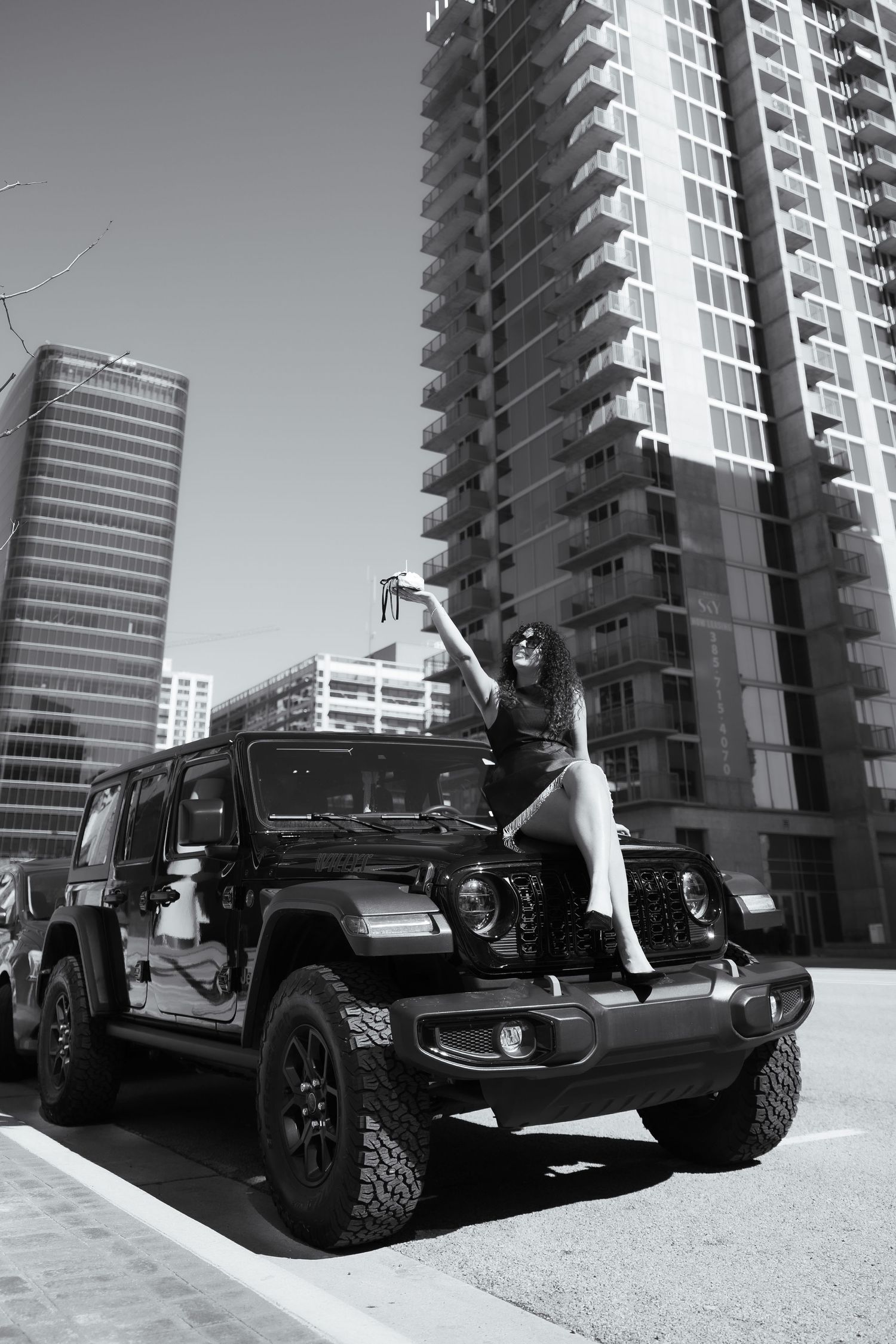 Black Jeep parked in front of modern high-rise buildings in black and white photography.