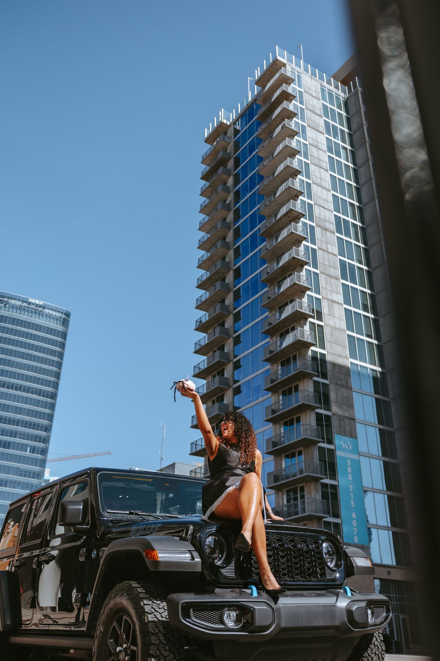 Black Jeep parked beside modern glass skyscraper on sunny day.
