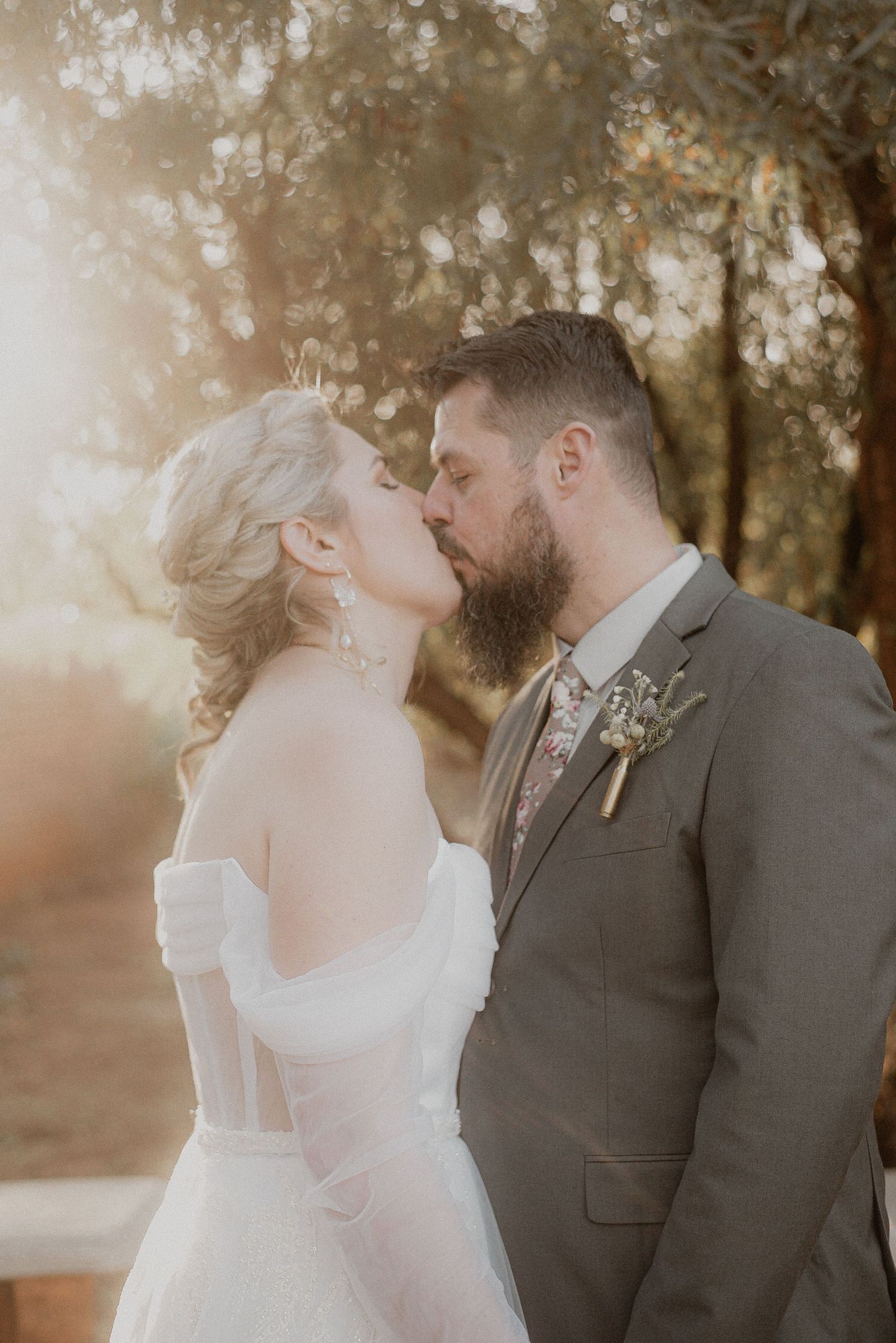 Wedding couple sharing tender moment in warm sunset lighting among trees.