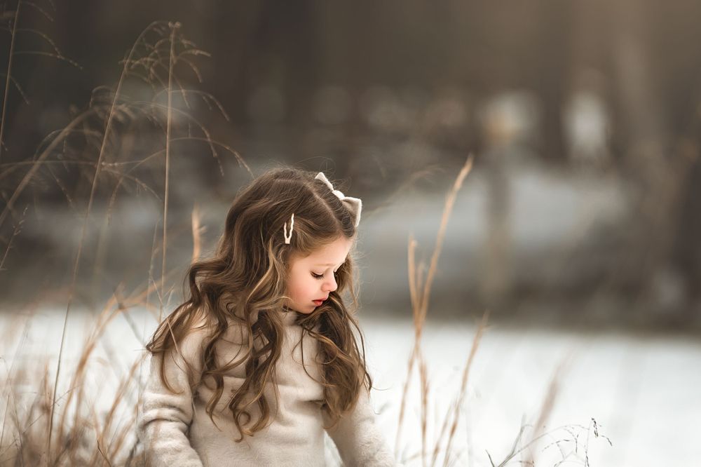 A person with long wavy hair wearing white sits outdoors in a dreamy winter setting with bokeh lighting effects.