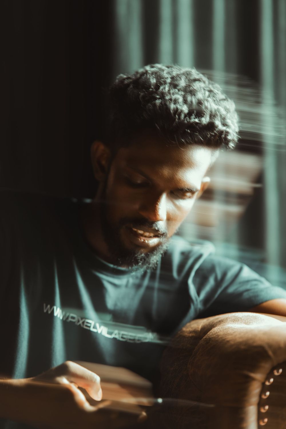 Moody portrait in dramatic lighting showing a figure in shadows wearing a dark t-shirt.