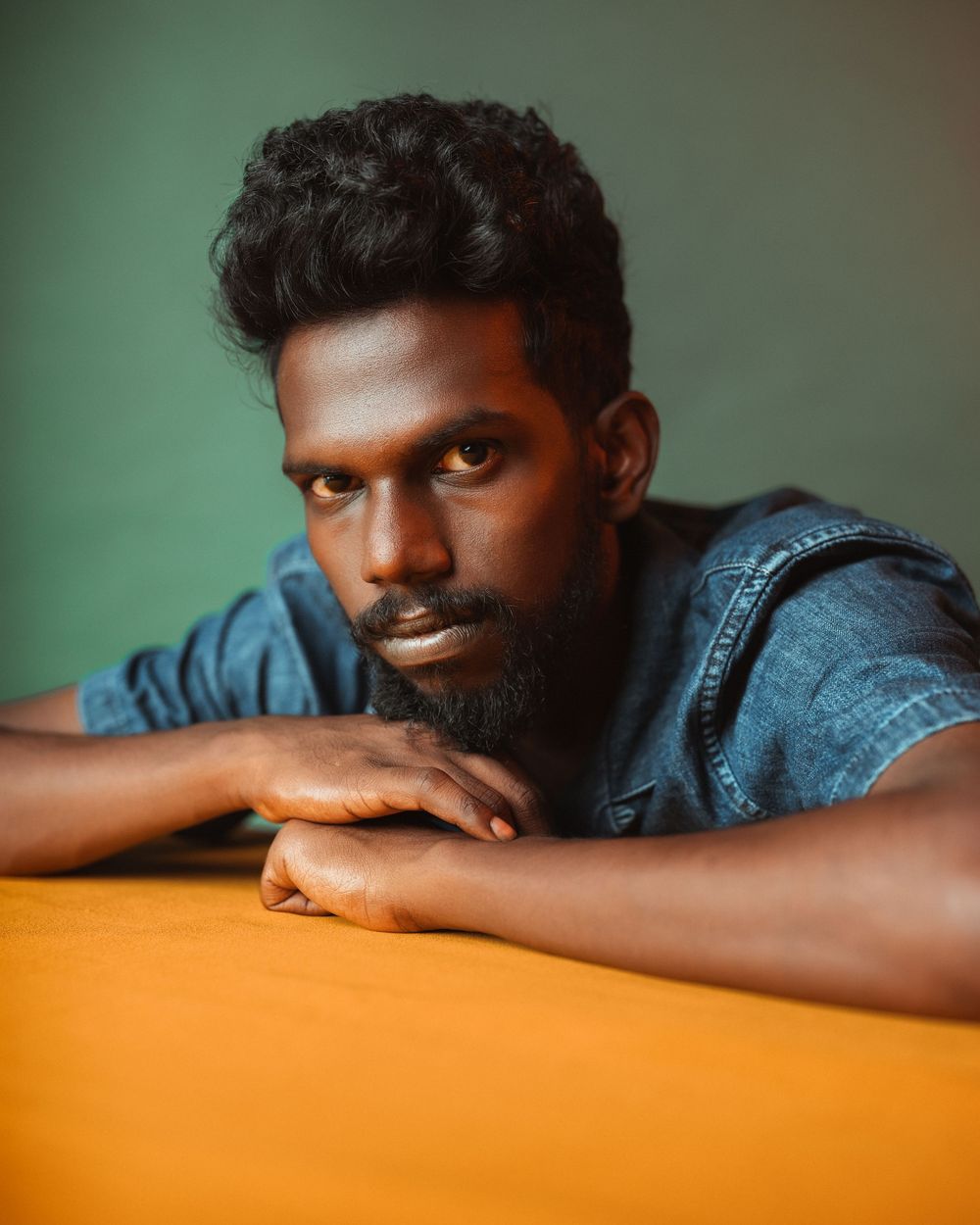 A person in denim rests their head on an orange surface creating a striking contrast between warm and cool tones.