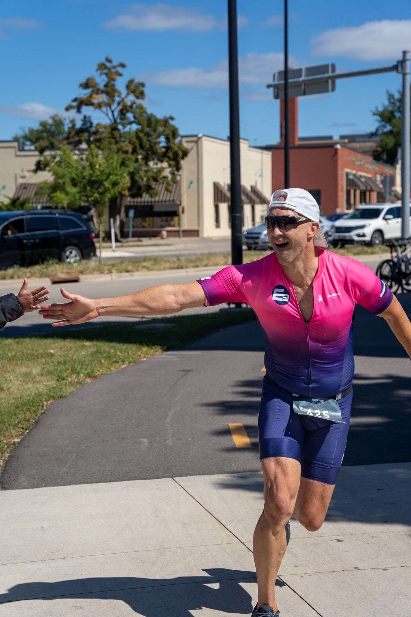 Athlete in pink top and navy shorts strikes joyful pose during outdoor race on sunny summer day.