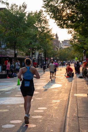 Runner on urban street at sunset with people walking along tree-lined path in golden evening light.