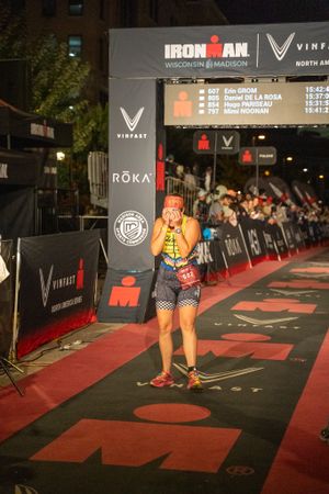 A competitor crosses the finish line at night during the Ironman Wisconsin triathlon in Madison with crowds cheering.