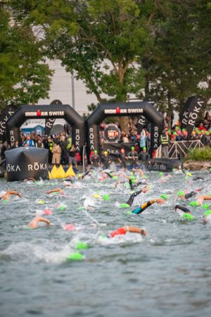 Swimmers compete in an Ironman triathlon event with black inflatable start gates visible in the background.