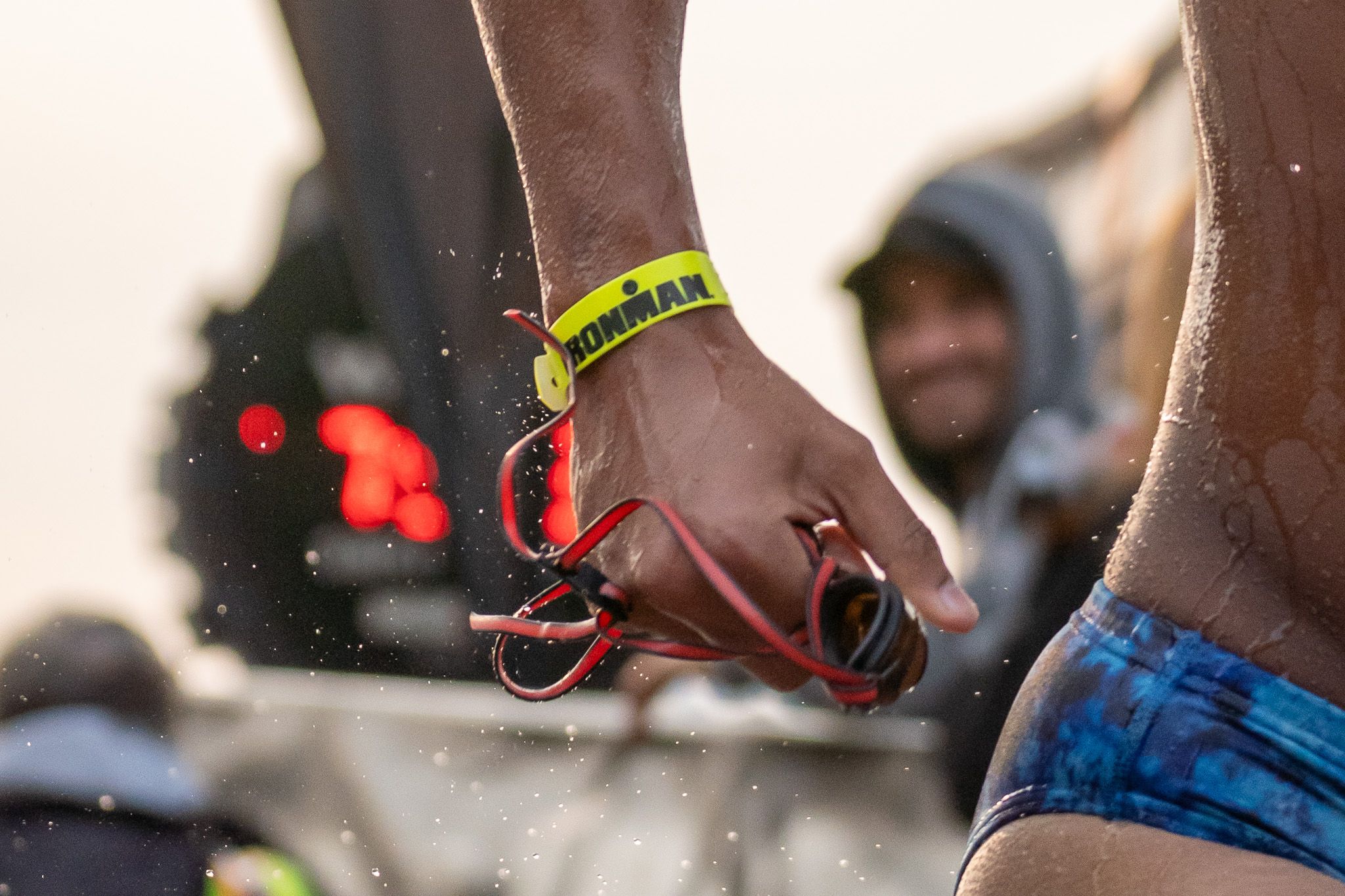 Close-up of hands wearing festival wristbands at an outdoor music event as the sun sets in the background.