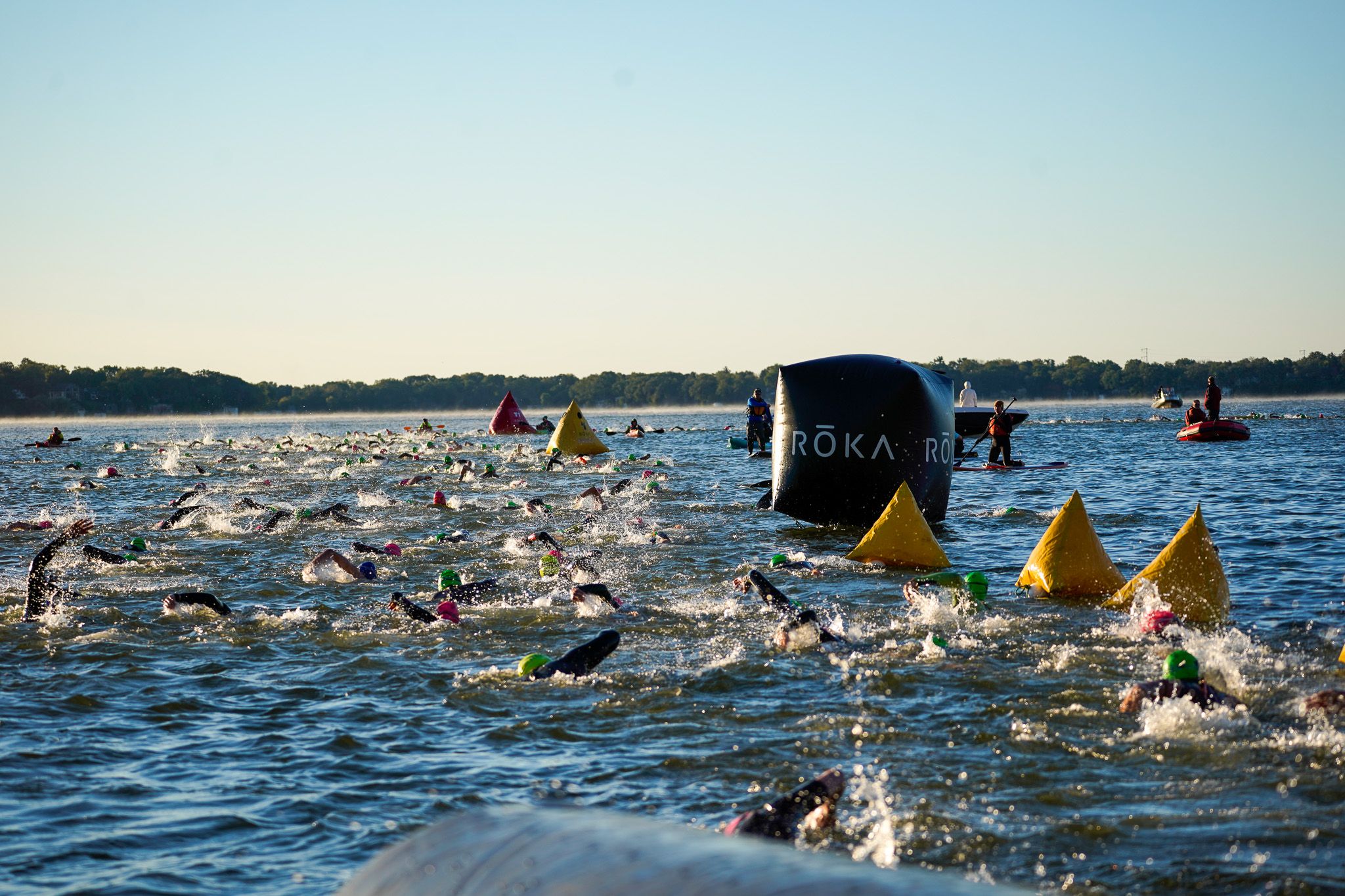 Athletes swim in open water during a triathlon race with yellow buoy markers visible.