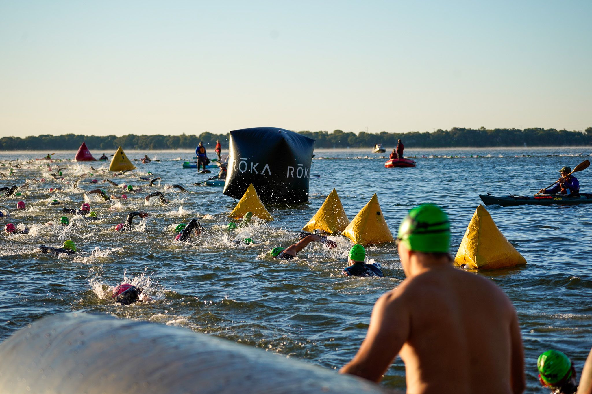 Athletes in swim caps follow bright yellow buoy markers during an open water triathlon competition.