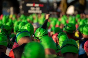 A crowd of people wearing bright green swim caps gathering before a swimming competition or triathlon event.