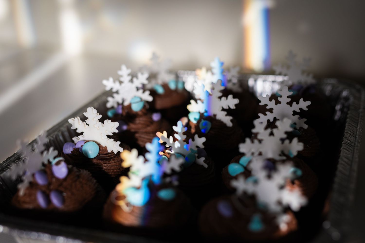 Close-up of chocolate cupcakes decorated with blue and silver snowflake sprinkles.