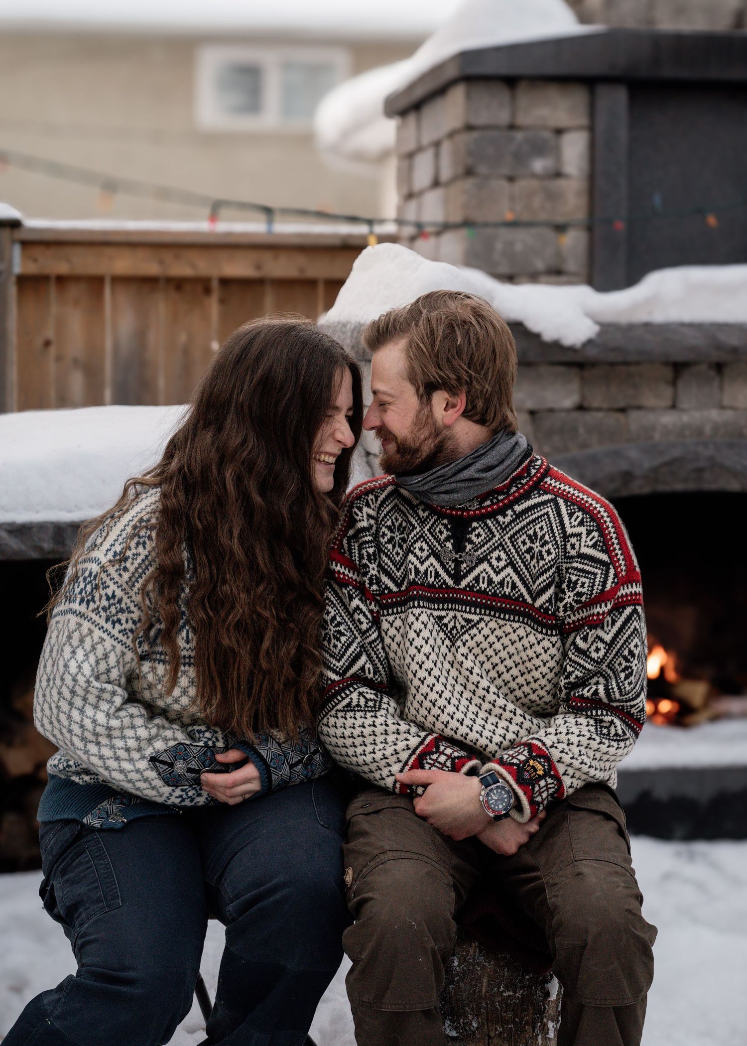 An intimate moment shared between a couple wearing matching winter sweaters by a stone fireplace.