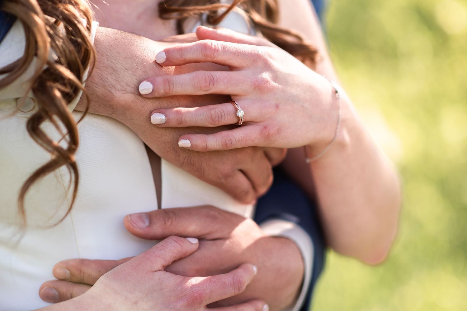 Close-up shot of hands embracing with an engagement ring on display in natural lighting.
