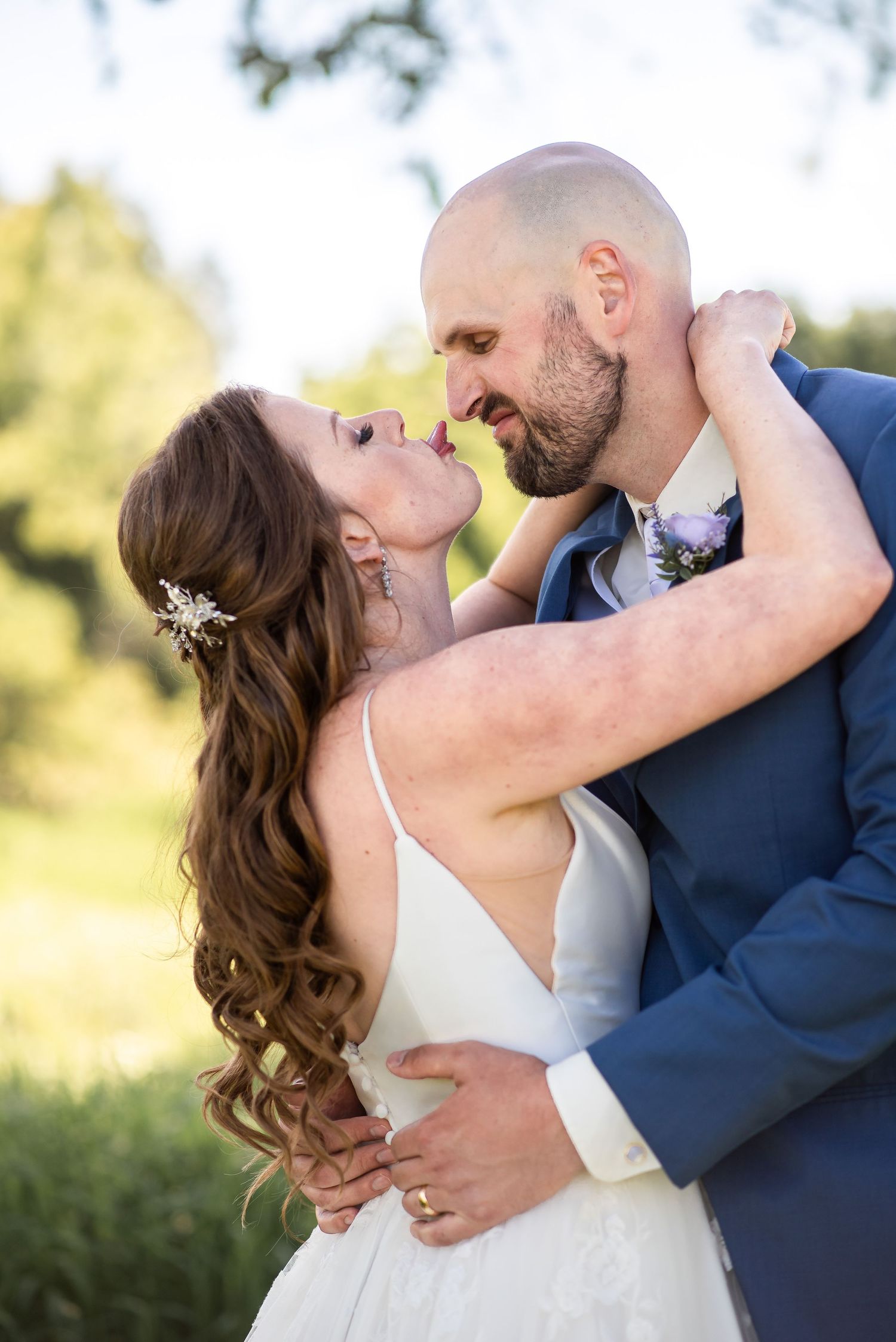 A romantic wedding couple embraces outdoors with the bride in white and groom in navy during an intimate moment.