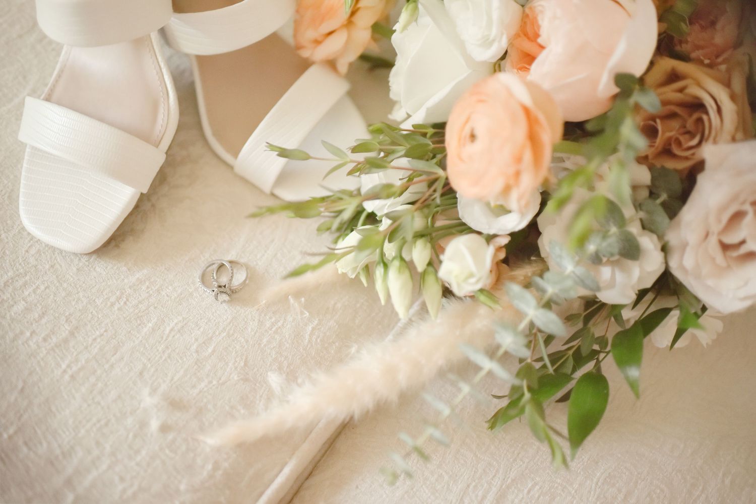 Elegant bridal bouquet with peach roses and white shoes on a cream surface.
