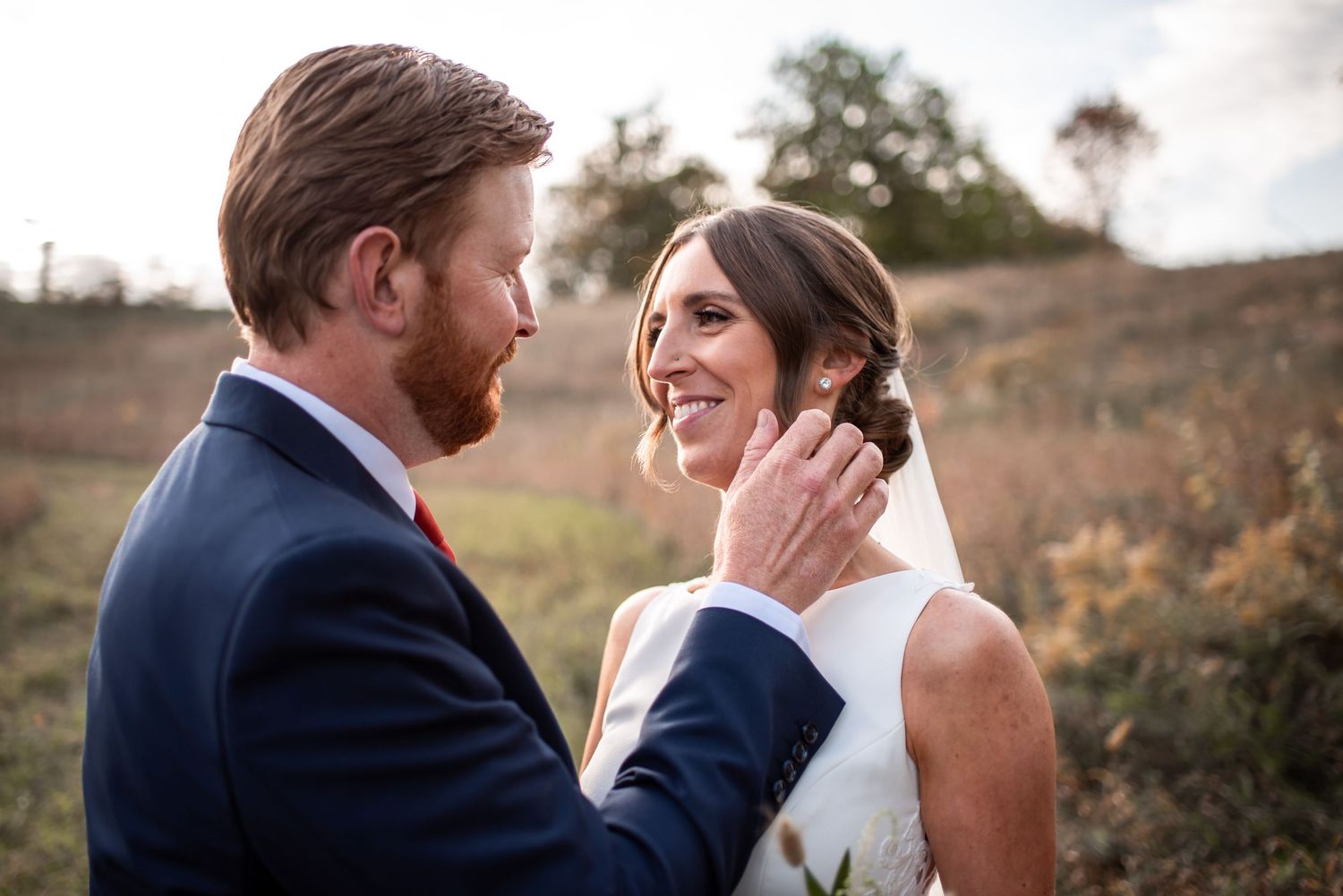 A romantic wedding moment captured outdoors with a couple sharing an intimate exchange in a natural setting.