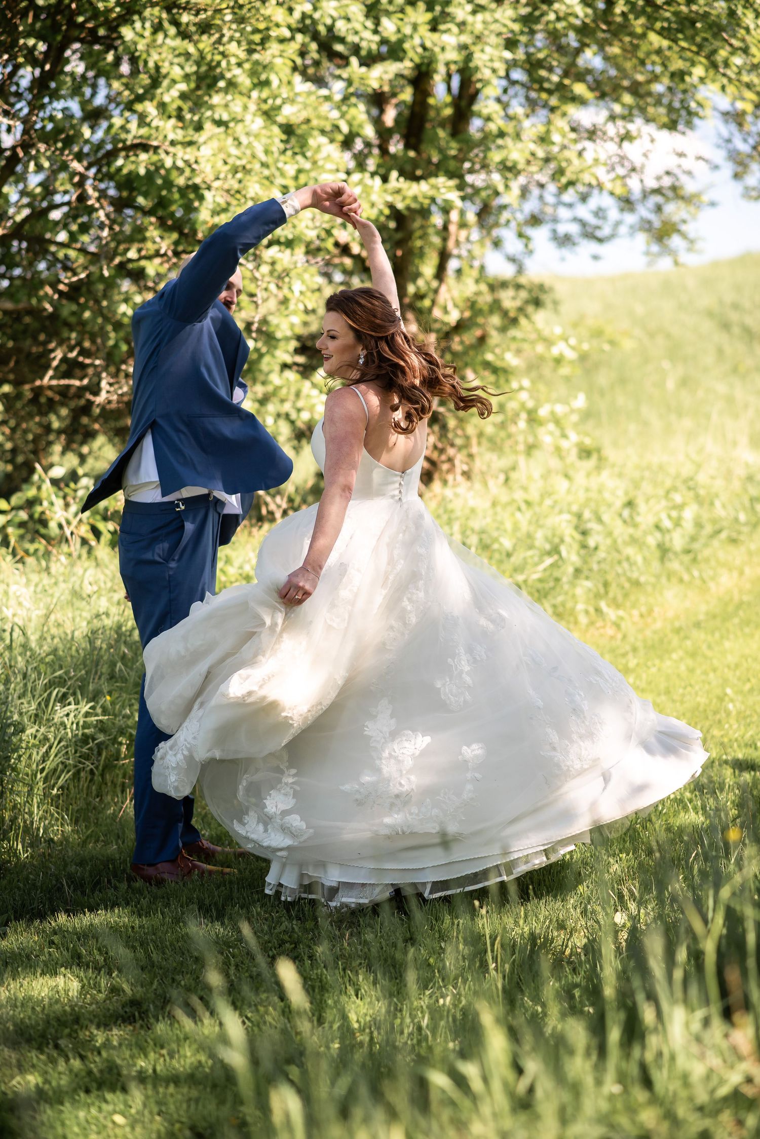 A couple dancing together in a sunlit meadow, the bride's elegant white gown swirling as they spin.