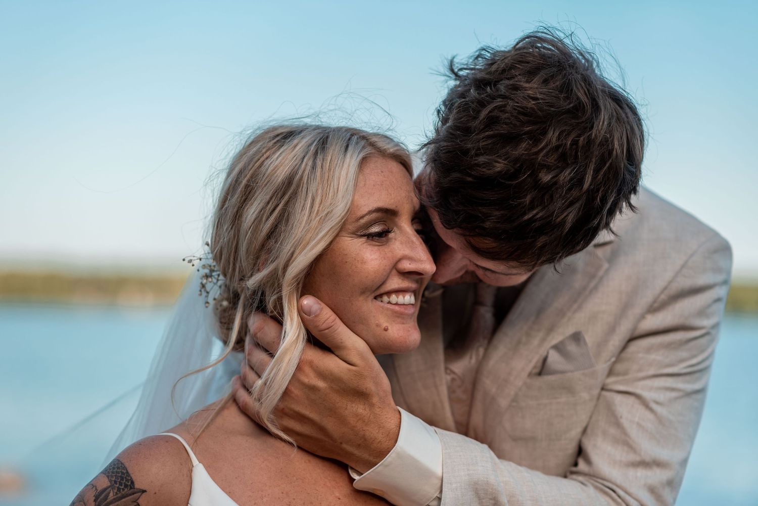 A sweet moment between newlyweds by the water as they share an intimate embrace during their outdoor wedding.