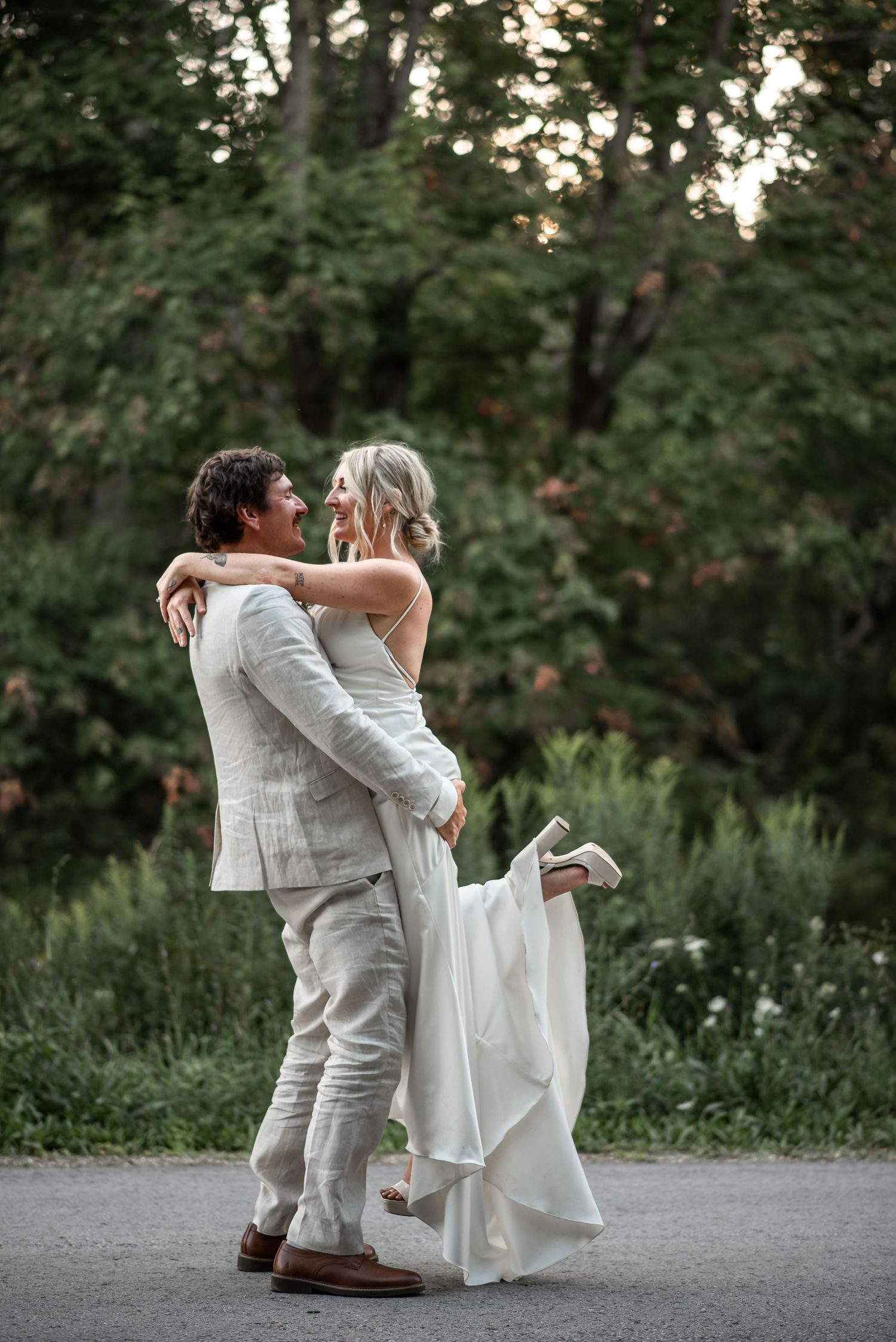 A joyful couple in wedding attire dances and embraces on a garden path at dusk.