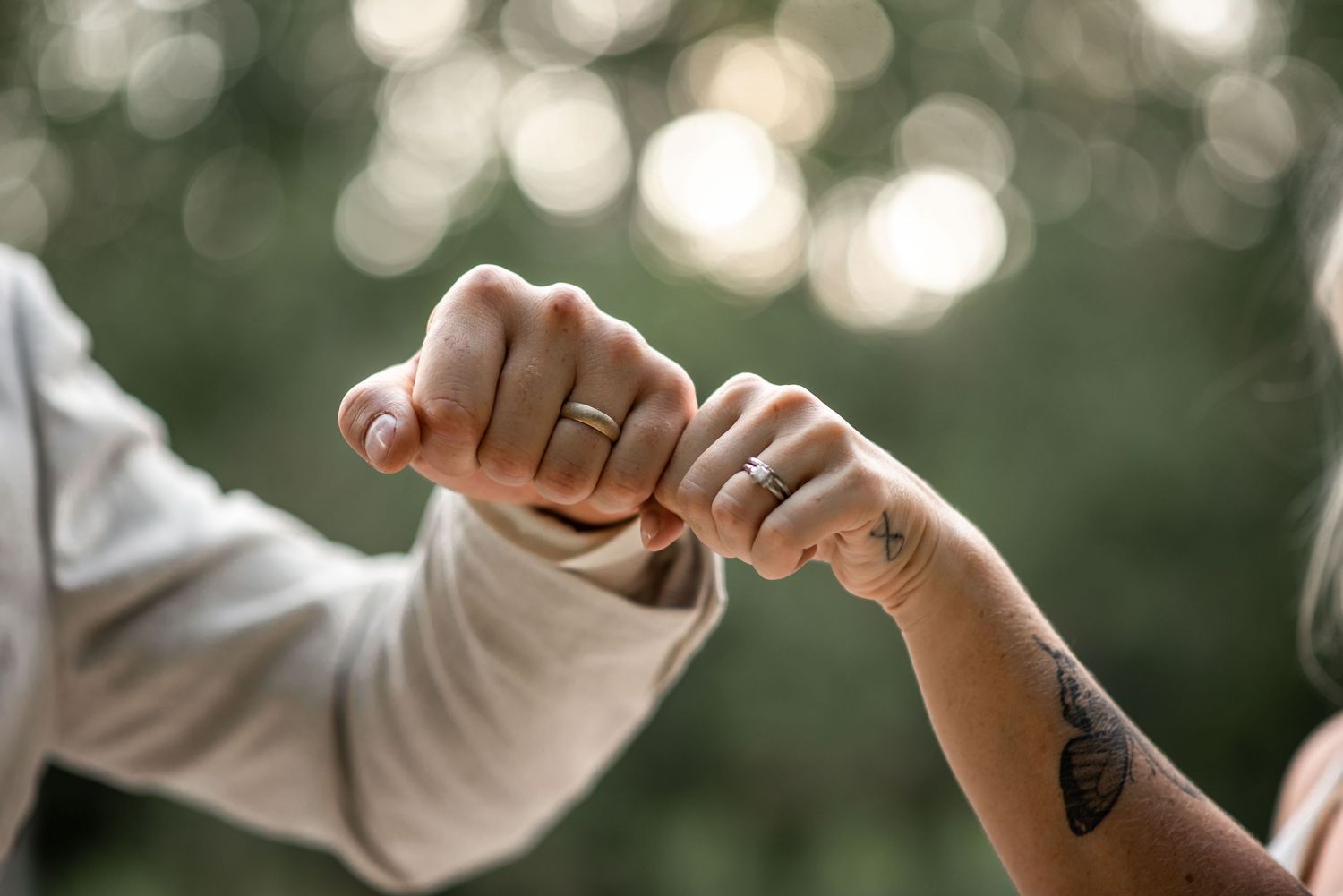 Two hands join together with interlocked pinky fingers making a promise against a blurred natural background.