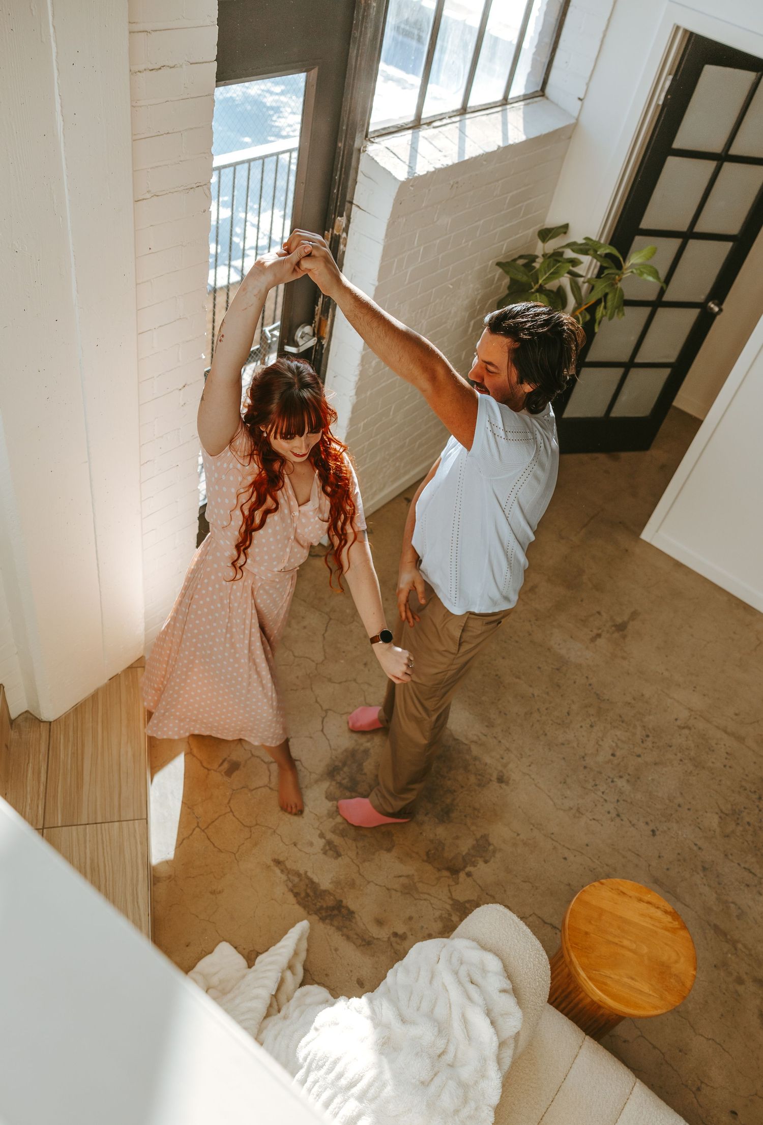 A couple dances together in a sunlit room with hardwood floors.