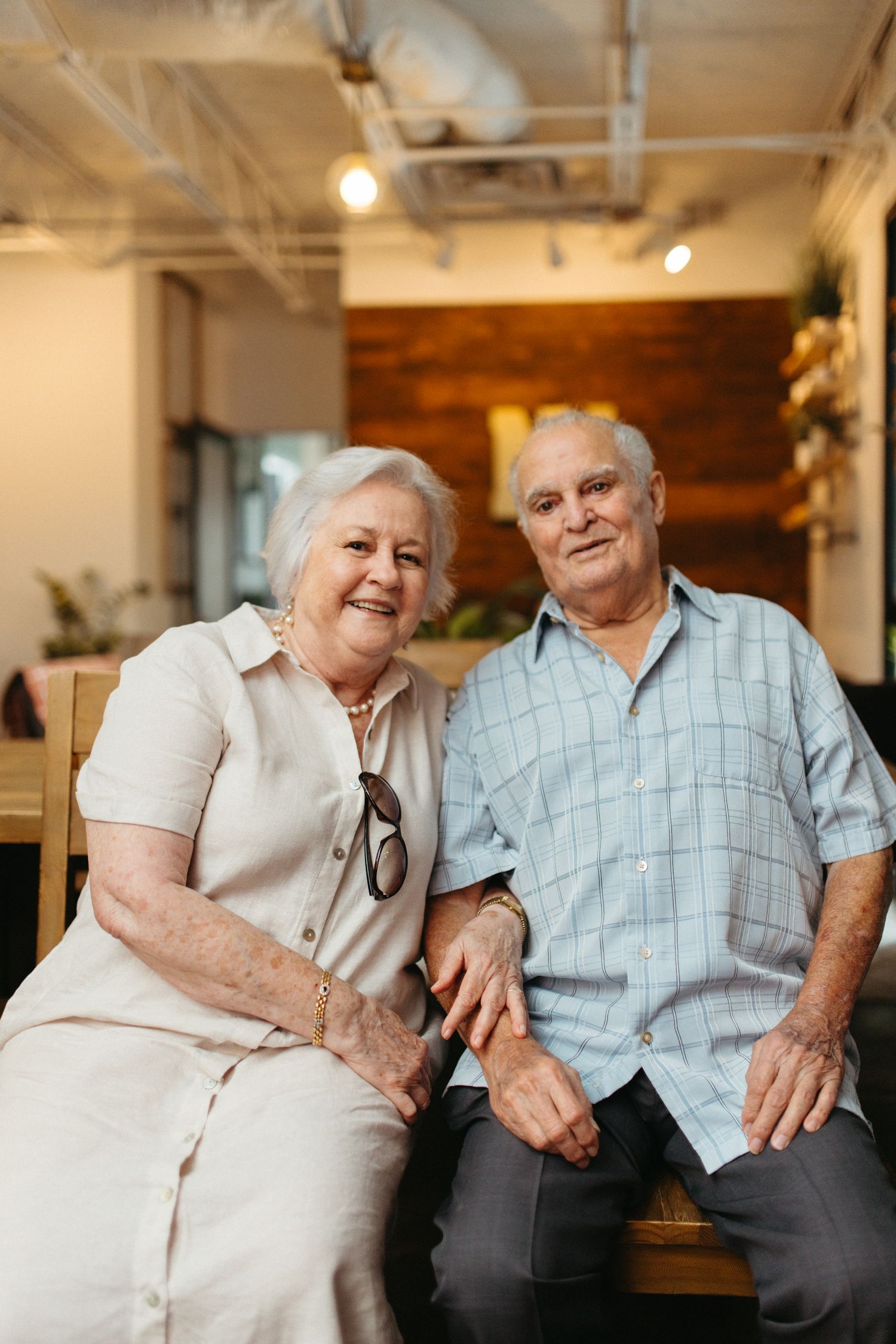 A loving elderly couple shares tender moments together while sitting on a couch in a bright indoor setting.