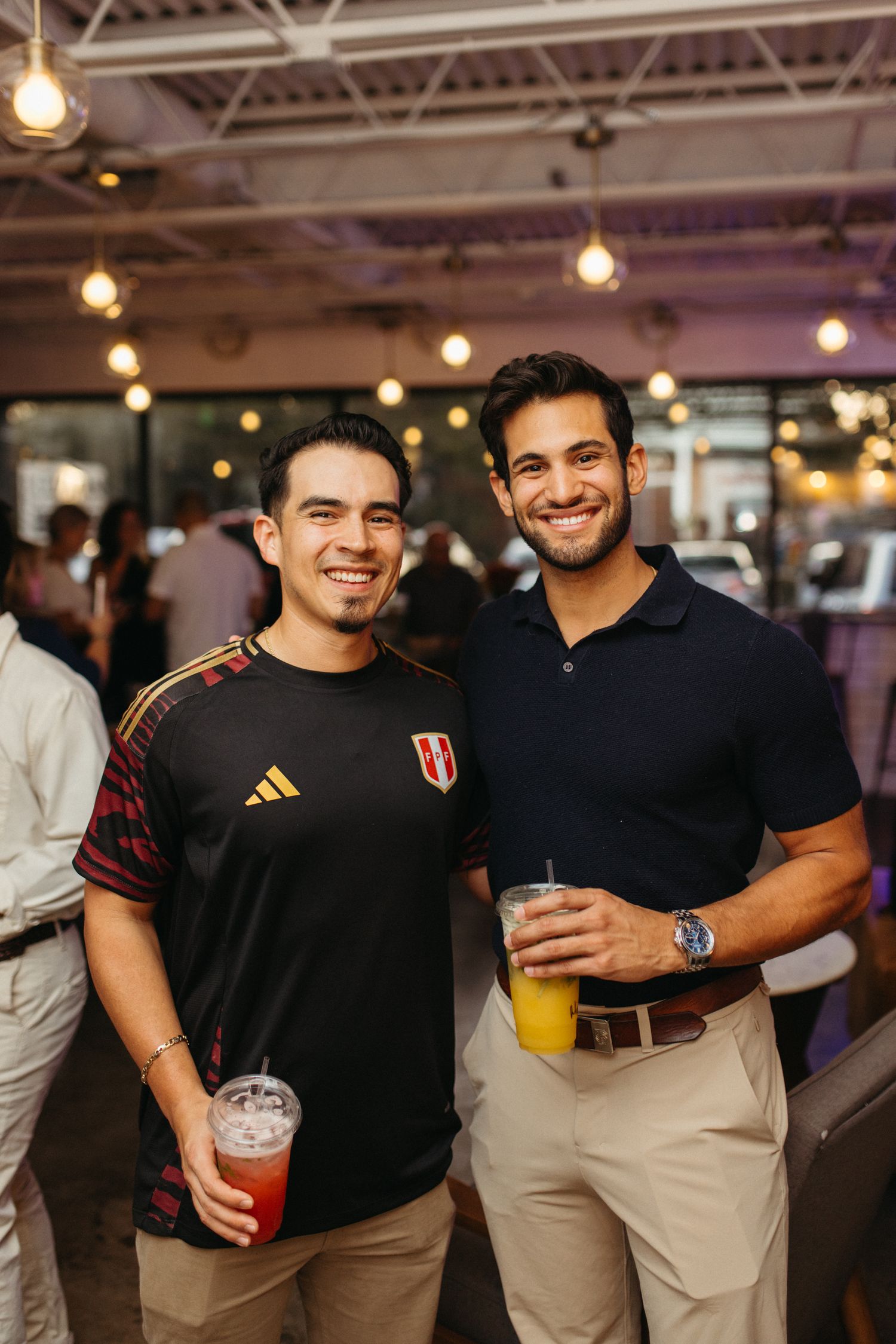 Group of friends enjoying drinks at a bar with hanging lights in the background.