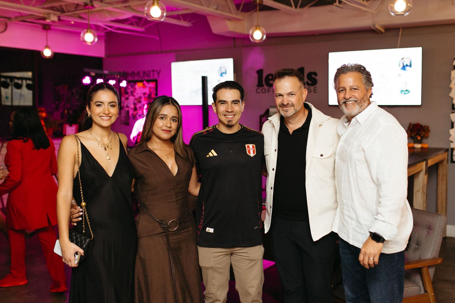 People gathered at an event with pink and purple lighting in what appears to be an indoor venue.