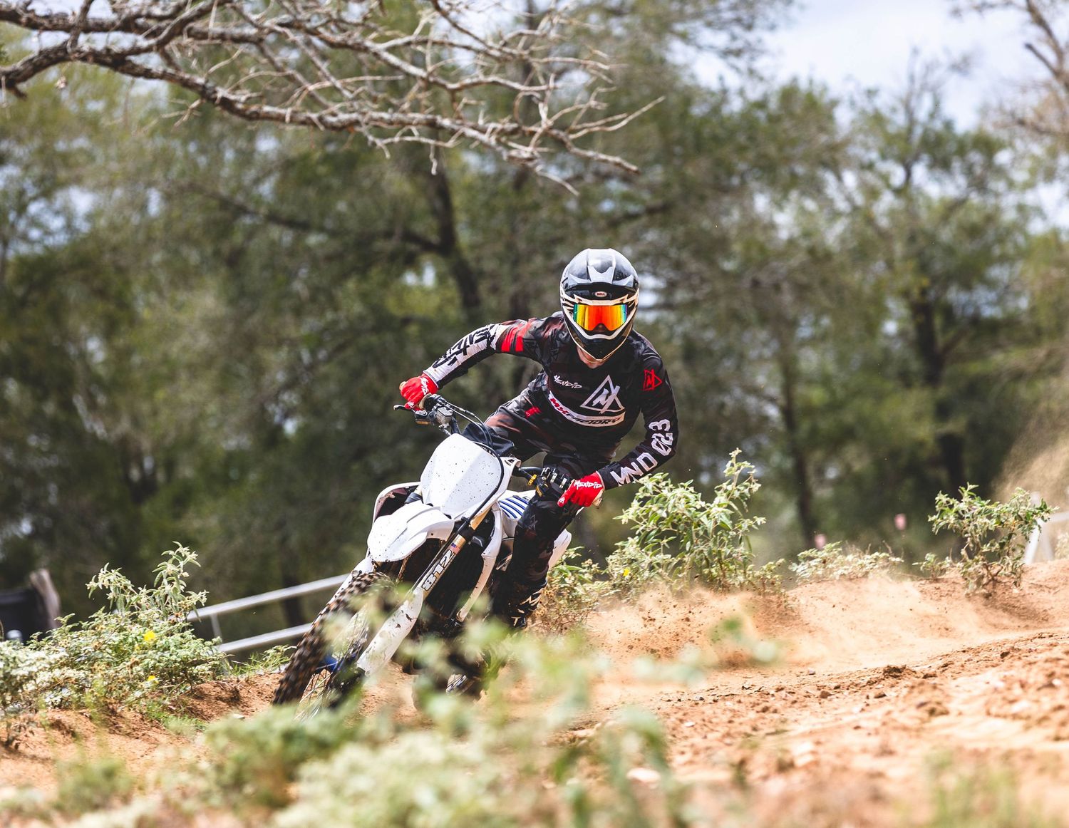 Dirt bike rider racing through wooded trail on white motorcycle.