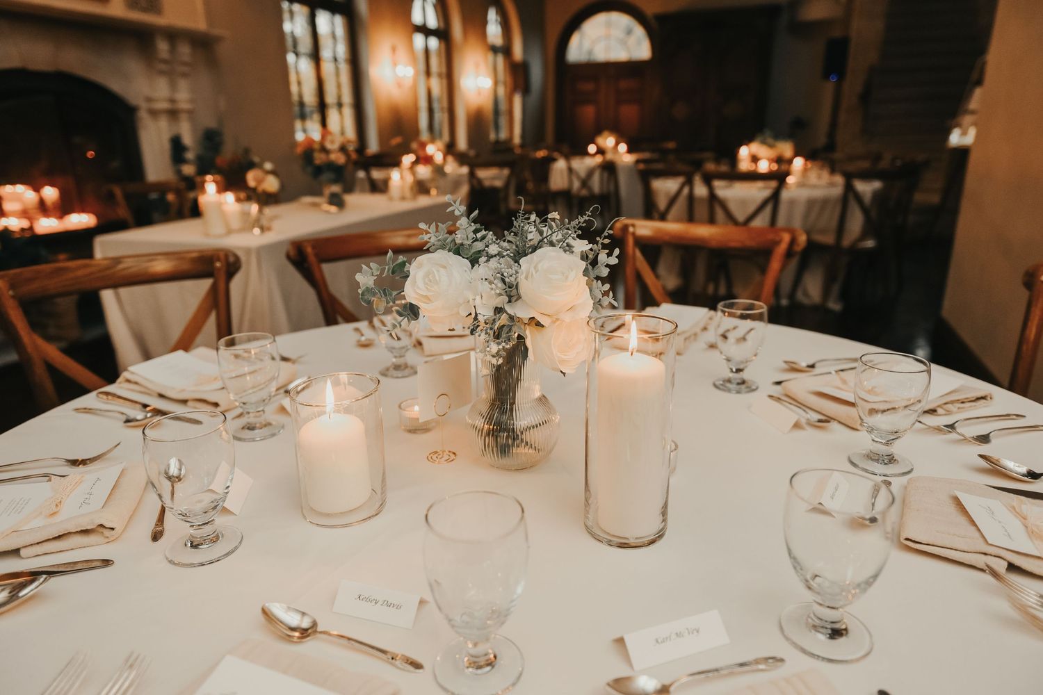Elegantly decorated round wedding reception table with white linens, glowing candles and delicate floral centerpiece.