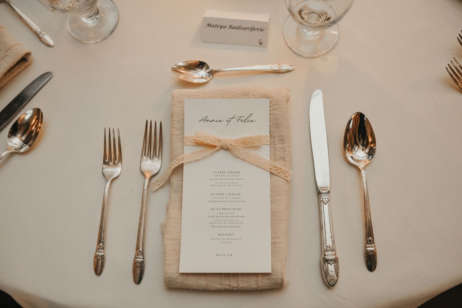 Elegant wedding table setting with wine glasses, silverware, and menu cards on a white tablecloth.