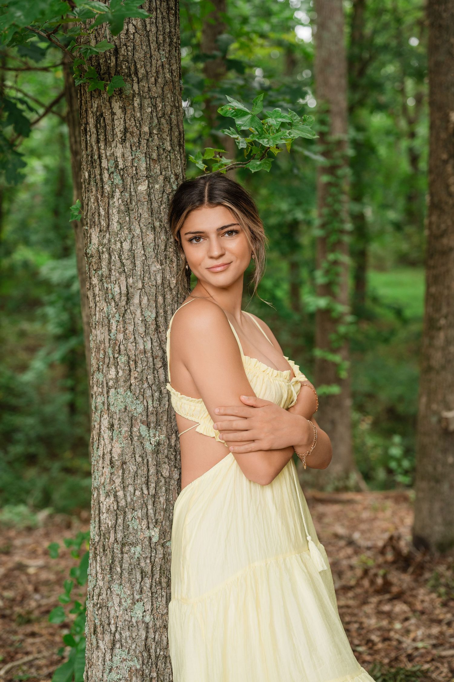 Outdoor portrait in pale yellow dress against forest backdrop.
