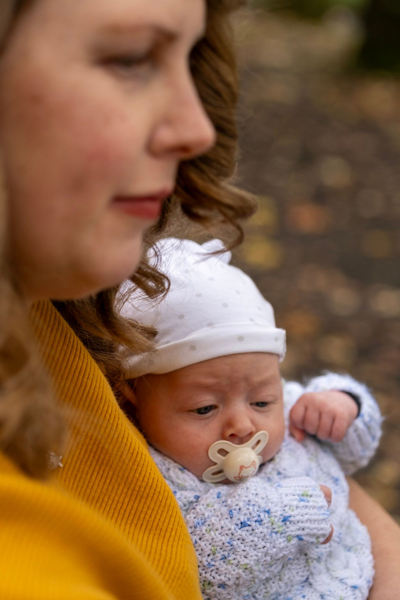 Baby with pacifier snuggles close in yellow sweater on autumn day.