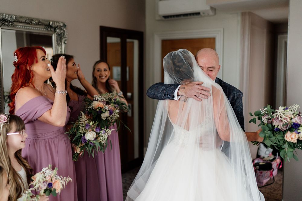 Emotional first look moment captured with bridesmaids in mauve dresses looking on.