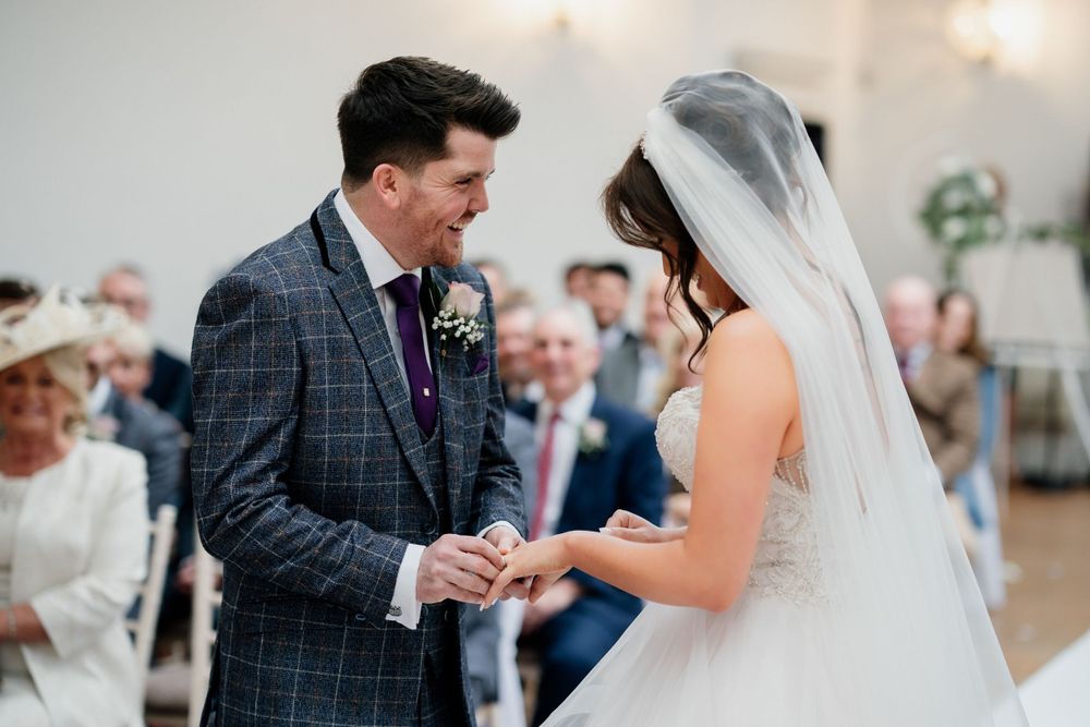 Exchange of rings during wedding ceremony at Barton Hall in bright indoor venue.