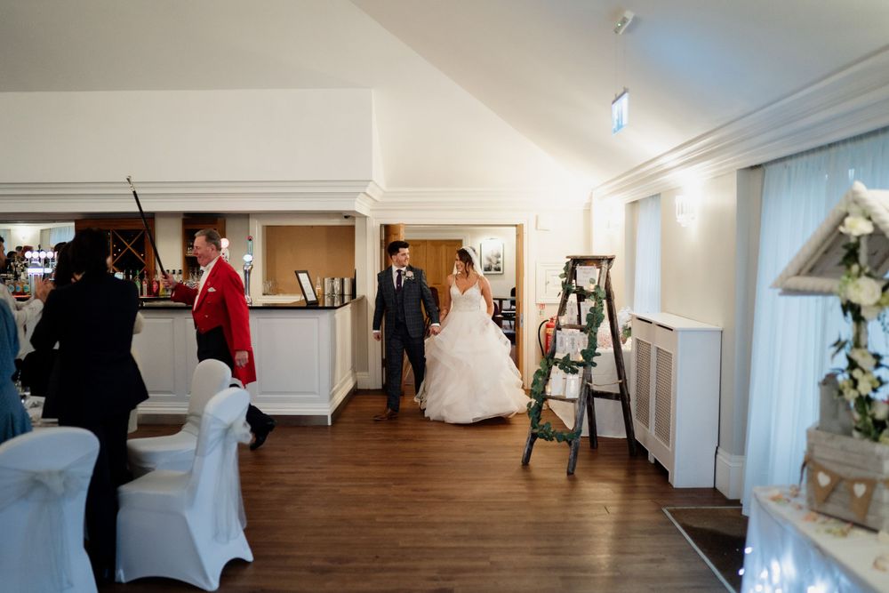 Wedding guests mingle in an elegant indoor reception venue with wooden floors and white decor.